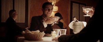 Movie still from “Lamborghini: The Man Behind the Legend” (2022), directed by Bobby Moresco – A man sitting at a table with a glass of wine; Medium shot, Over the shoulder angle