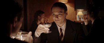 Movie still from “Lamborghini: The Man Behind the Legend” (2022), directed by Bobby Moresco – A man in a suit holding a glass of wine; Close Up shot, Over the shoulder angle