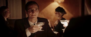 Movie still from “Lamborghini: The Man Behind the Legend” (2022), directed by Bobby Moresco – A man and a woman are holding drinks in their hands; Close Up shot, Over the shoulder angle