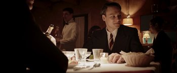 Movie still from “Lamborghini: The Man Behind the Legend” (2022), directed by Bobby Moresco – A man sitting at a dinner table in front of two other men; Medium shot, Over the shoulder angle