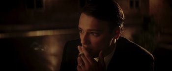 Movie still from “Lamborghini: The Man Behind the Legend” (2022), directed by Bobby Moresco – A man in a suit and tie holding his hand to his face; Close Up shot, Low angle