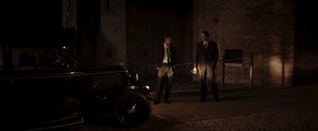 Movie still from “Lamborghini: The Man Behind the Legend” (2022), directed by Bobby Moresco – A couple of men standing next to each other on a sidewalk; Wide shot, Low angle