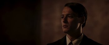 Movie still from “Lamborghini: The Man Behind the Legend” (2022), directed by Bobby Moresco – A person wearing a suit and tie; Close Up shot, Low angle