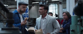 Movie still from “Lamborghini: The Man Behind the Legend” (2022), directed by Bobby Moresco – A man in a suit and tie holding a box of food; Medium shot, Over the shoulder angle