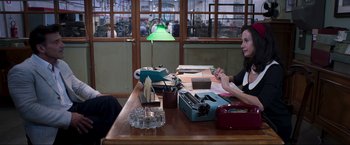 Movie still from “Lamborghini: The Man Behind the Legend” (2022), directed by Bobby Moresco – A woman sitting at a table with a typewriter; Medium shot, Over the shoulder angle