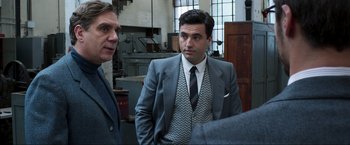 Movie still from “Lamborghini: The Man Behind the Legend” (2022), directed by Bobby Moresco – A man in a suit and tie standing next to another man in a suit and tie; Medium shot, Over the shoulder angle