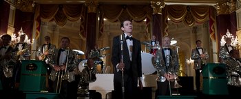 Movie still from “Lamborghini: The Man Behind the Legend” (2022), directed by Bobby Moresco – A man in a tuxedo is holding a microphone; Medium shot, Low angle