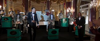 Movie still from “Lamborghini: The Man Behind the Legend” (2022), directed by Bobby Moresco – A group of men dressed up in silver suits and tuxedos; Wide shot, Low angle