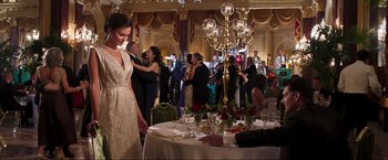Movie still from “Lamborghini: The Man Behind the Legend” (2022), directed by Bobby Moresco – A woman in a white dress standing in front of a table; Wide shot, Over the shoulder angle