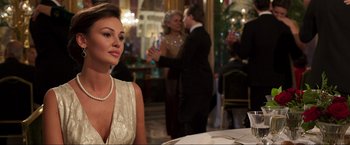 Movie still from “Lamborghini: The Man Behind the Legend” (2022), directed by Bobby Moresco – A beautiful woman in a white dress sitting at a table; Medium shot, Over the shoulder angle