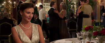 Movie still from “Lamborghini: The Man Behind the Legend” (2022), directed by Bobby Moresco – A woman sitting at a table in front of other people in a room; Medium shot, Over the shoulder angle