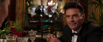 Movie still from “Lamborghini: The Man Behind the Legend” (2022), directed by Bobby Moresco – A person sitting at a table with a glass of wine; Close Up shot, Over the shoulder angle