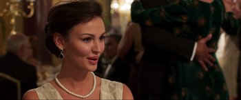Movie still from “Lamborghini: The Man Behind the Legend” (2022), directed by Bobby Moresco – A woman wearing a white dress and a pearl necklace; Close Up shot, Over the shoulder angle