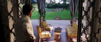 Movie still from “Lamborghini: The Man Behind the Legend” (2022), directed by Bobby Moresco – A man standing on a porch looking at a lawn; Extreme Wide shot, Over the shoulder angle
