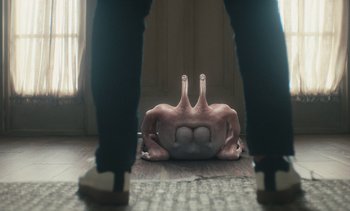 Movie still from “Landscape with Invisible Hand” (2023), directed by Cory Finley – A person standing in front of an upside - down object; Extreme Close Up shot, Low angle