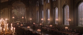 Movie still from “Lara Croft: Tomb Raider” (2001), directed by Simon West – People are sitting at tables in a large room; Extreme Wide shot, High angle