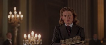 Movie still from “Lara Croft: Tomb Raider” (2001), directed by Simon West – A man in a suit and tie holding a bunch of papers; Medium shot, Over the shoulder angle