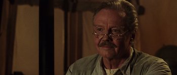 Movie still from “Lara Croft: Tomb Raider” (2001), directed by Simon West – An older man with a mustache wearing glasses; Close Up shot, Over the shoulder angle