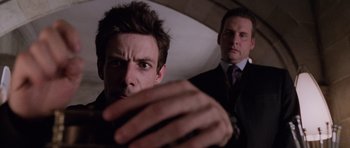 Movie still from “Lara Croft: Tomb Raider” (2001), directed by Simon West – Two men in business suits are looking at the camera; Close Up shot, Low angle
