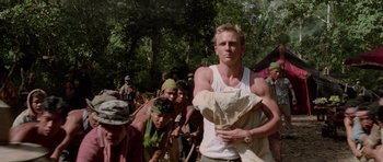 Movie still from “Lara Croft: Tomb Raider” (2001), directed by Simon West – A group of people in the woods with a man in a white tank top; Medium shot, Low angle