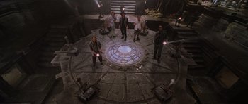 Movie still from “Lara Croft: Tomb Raider” (2001), directed by Simon West – A group of people standing in a circle with lights on them; Wide shot, High angle