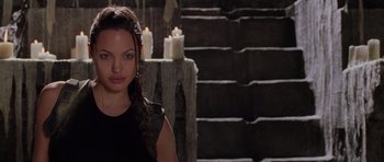 Movie still from “Lara Croft: Tomb Raider” (2001), directed by Simon West – A woman standing in front of some steps with candles; Close Up shot, Over the shoulder angle