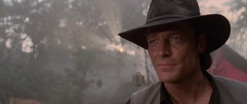 Movie still from “Lara Croft: Tomb Raider” (2001), directed by Simon West – A person wearing a hat with trees in the background; Close Up shot, Over the shoulder angle
