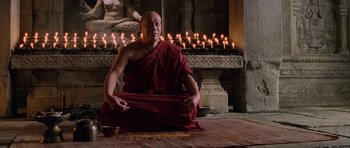 Movie still from “Lara Croft: Tomb Raider” (2001), directed by Simon West – A man sitting on the ground in front of candles; Medium shot, Low angle