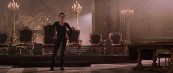 Movie still from “Lara Croft: Tomb Raider” (2001), directed by Simon West – A woman standing in front of a group of chairs in a room; Wide shot, Low angle