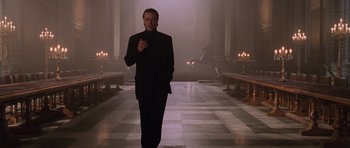Movie still from “Lara Croft: Tomb Raider” (2001), directed by Simon West – A man in a black suit standing in front of a row of candles; Medium shot, Low angle