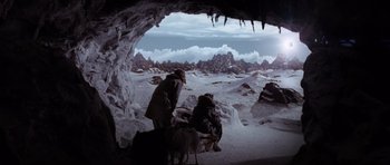 Movie still from “Lara Croft: Tomb Raider” (2001), directed by Simon West – A group of people standing inside of a cave with mountains in the background; Wide shot, High angle