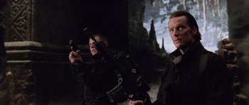 Movie still from “Lara Croft: Tomb Raider” (2001), directed by Simon West – A man holding a gun while standing next to another man holding a gun; Medium shot, Low angle
