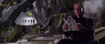 Movie still from “Lara Croft: Tomb Raider” (2001), directed by Simon West – A man sitting on the ground holding a piece of paper; Medium shot, Low angle