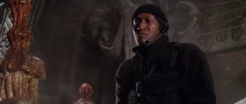 Movie still from “Lara Croft: Tomb Raider” (2001), directed by Simon West – A man in a black jacket standing in front of a statue; Close Up shot, Low angle