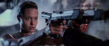 Movie still from “Lara Croft: Tomb Raider” (2001), directed by Simon West – A woman holding a gun while a man holds a gun; Close Up shot, Over the shoulder angle