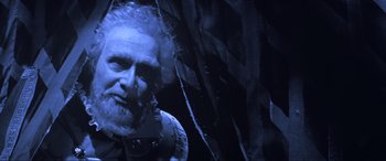 Movie still from “Last Action Hero” (1993), directed by John McTiernan – An old man with a long beard is standing next to a tree; Medium shot, Low angle