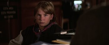 Movie still from “Last Action Hero” (1993), directed by John McTiernan – A boy sitting in front of a desk with a book; Close Up shot, Over the shoulder angle