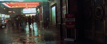 Movie still from “Last Action Hero” (1993), directed by John McTiernan – A man walking down a street next to a building; Extreme Wide shot, High angle