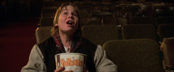 Movie still from “Last Action Hero” (1993), directed by John McTiernan – A young boy holding a bucket of popcorn in a movie theater; Close Up shot, Low angle