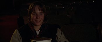Movie still from “Last Action Hero” (1993), directed by John McTiernan – A young man sitting in a movie theater holding a drink; Close Up shot, High angle