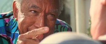 Movie still from “Last Action Hero” (1993), directed by John McTiernan – An older man is looking at the camera with his finger in his mouth; Extreme Close Up shot, Over the shoulder angle
