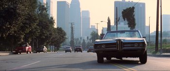 Movie still from “Last Action Hero” (1993), directed by John McTiernan – Cars driving down a street in the middle of a city; Wide shot, Low angle