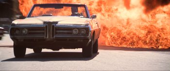 Movie still from “Last Action Hero” (1993), directed by John McTiernan – A car is on a road with a fire coming out of it; Wide shot, Low angle