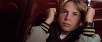 Movie still from “Last Action Hero” (1993), directed by John McTiernan – A young man sitting on a chair with his hand on his head; Close Up shot, High angle