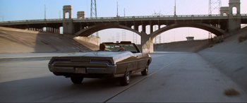 Movie still from “Last Action Hero” (1993), directed by John McTiernan – A car driving down a street next to a bridge; Wide shot, High angle
