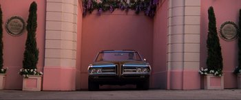 Movie still from “Last Action Hero” (1993), directed by John McTiernan – A car parked in front of a pink building; Wide shot, Low angle
