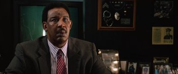 Movie still from “Last Action Hero” (1993), directed by John McTiernan – A man wearing a suit and tie sitting in front of a mirror; Close Up shot, Low angle