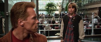 Movie still from “Last Action Hero” (1993), directed by John McTiernan – A man and a boy in a crowded room; Medium shot, Over the shoulder angle