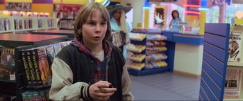 Movie still from “Last Action Hero” (1993), directed by John McTiernan – A young boy holding a cell phone in his hand; Medium shot, Over the shoulder angle