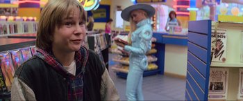Movie still from “Last Action Hero” (1993), directed by John McTiernan – A boy and a girl dressed up in a store; Medium shot, Over the shoulder angle